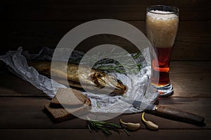 Traditional Siberian smoked fish wrapped in the wrinkles paper lie on the wood table near the damask knife and the bread