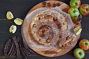 Traditional sliced apple pie with spices on the brown wooden board. Apple pie decorated with fresh apples, carob pods, anise stars