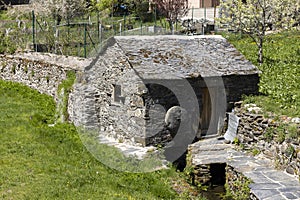 Traditional small stone water mill on a bright sunny spring day next to stream with green vegetation in Tormaleo village Asturias
