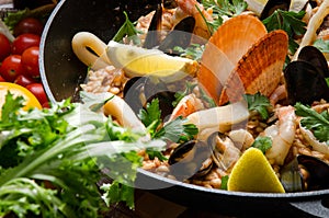 Traditional Spanish dish Paella with seafood: shrimps, squids, mussels, wine, lemon and rice in a black cauldron