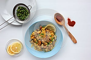 Traditional Spanish seafood dish paella with ingredients, lemon slice and wooden spoon with red paprika powder on table.