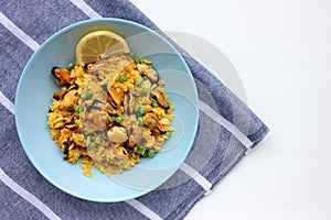 Traditional Spanish seafood dish paella with ingredients on table. Mussel risotto with green peas and lemon slice  on blue plate