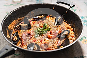 Traditional spanish seafood paella or arroz caldoso inside black pan with shrimps, mussels, clams and parsley. Homemade