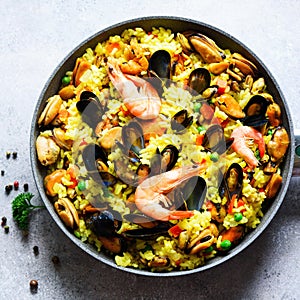 Traditional spanish seafood paella in pan rice, peas, shrimps, mussels, squid on light grey concrete background. Top