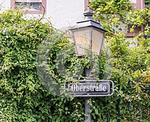 A traditional street lantern with street name attached, surrounded by lush greenery in Rudesheim on the Rhine in Germany