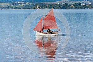 Traditional style red sails on small yacht becalmed in bay