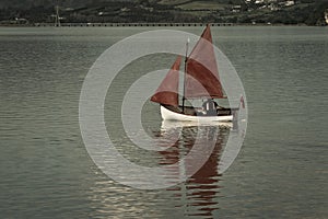 Traditional style red sails on small yacht becalmed in bay