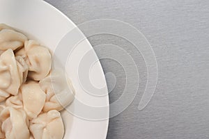 Traditional tasty boiled russian pelmeni, ravioli, dumplings with meat on white ceramic plate on grey background, copy space