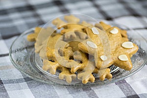 Traditional tasty Czech gingerbreads, Christmas snowflakes and star on glass plate on grey chequered tablecloth