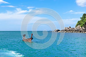 Traditional Thai boat is anchored near a small rocky island in a calm sea on a sunny day