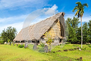 Traditional thatched yapese men`s meeting house faluw or fale and a bank of stone money rai. Yap island, Micronesia, Oceania.