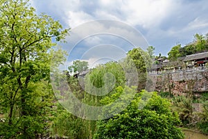 Traditional tile-roofed buildings on riverside cliff in cloudy s