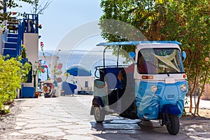 Traditional tuk-tuk moto taxi is waiting for passengers on empty road to sea at resort. Popular three-wheeler vehicle in