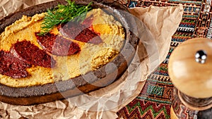 Traditional Turkish, Arabic cuisine. Hummus with salami sausage, in a clay plate, with parchment on a wood table