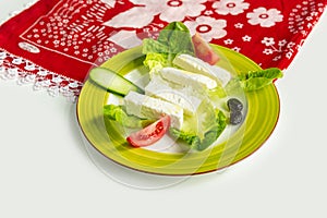 Traditional Turkish Cheese or Beyaz Peynir with cucumber and tomato in dish isolated on colorful table cloth top view on grey