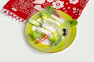 Traditional Turkish Cheese or Beyaz Peynir with cucumber and tomato in dish isolated on colorful table cloth top view on grey