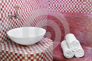 Traditional Turkish hamam with stone walls, sink and stack of towels