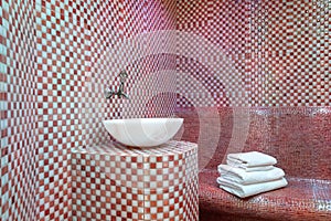Traditional Turkish hamam with stone walls, sink and stack of towels