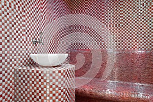 Traditional Turkish hamam with stone walls, sink and stack of towels