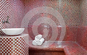 Traditional Turkish hamam with stone walls, sink and stack of  towels