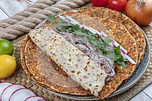 Traditional Turkish pizza, called Lahmacun, being prepared with meat, onion and parsley, displayed on a wooden table at a a street