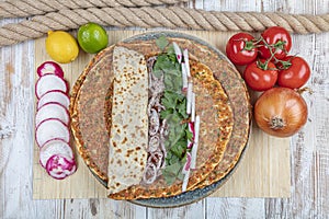 Traditional Turkish pizza, called Lahmacun, being prepared with meat, onion and parsley, displayed on a wooden table at a a street