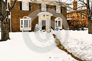 Traditional two story brick house with bay windows and pillared porch in the snow with the sidewalk cleared