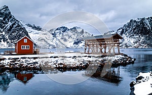 Traditional typical red rorbu house and wooden construction for drying codfish in the fishing village in Lofoten islands, Norway.