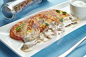 Traditional Ukrainian and Belarusian dish - fried potato pancakes draniki, deruny with sour cream and porcini mushrooms, served