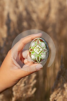 A traditional Ukrainian Easter egg in green-brown colors is held in the hand on a background of hay