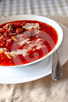 traditional Ukrainian-Russian tomato borscht soup with sour cream in a white plate on the table. View from above