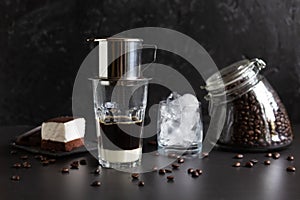 Traditional vietnamese coffee maker placed on the top of glass, glass jar with coffee beans, glass with ice and souffle dessert