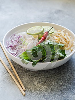 Traditional Vietnamese soup- pho ga in white bowl with chicken and rice noodles, mint and cilantro, green and red onion, chili,