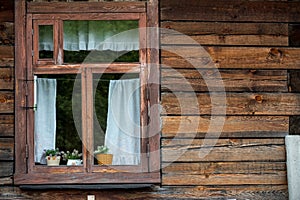 Traditional vintage old brown wooden frame window with curtains and flowers on wooden wall