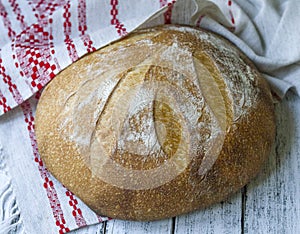 Traditional wheat freshly rustic baked bread with whole grain flour on white wooden background with national linen