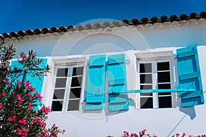 Traditional white greek white with blue window shutter in Mediterraneanstyle and rosa flowers. Fiskardo, Kefalonia