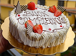 Traditional white Italian birthday cake with congratilations, buon compleanno means happy birthday photo