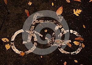 A traditional white road sign, bicycle symbol, on the dark cement. This symbol sign is specified that this lane of the road is for