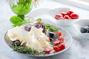 Traditional white soft fibrous Cecil cheese lies on a plate. The cheese is decorated with ripe tomatoes and olives