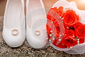 Traditional white wedding shoes with rings near bridal bouguet.