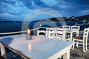 Traditional white wooden tables and chairs of a greek tavern at night and the view of the beach of Amaliapoli, Greece