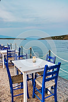 Traditional white wooden tables and chairs of a greek tavern at night and the view of the beach of Amaliapoli, Greece