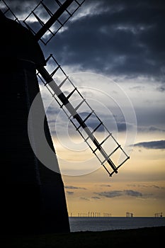 Traditional windmill silhouetted against modern offshore wind farm