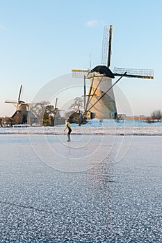 Traditional windmills and frozen canal with female skater, Kinderdijk, Netherlands