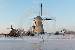 Traditional windmills and frozen canal with lonely skater, Kinderdijk, Netherlands