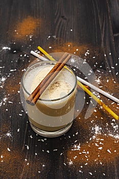 Traditional winter eggnog with milk, rum and cinnamon, sprinkle with grated nutmeg. Cocktail straws, dark wooden background