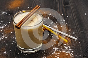 Traditional winter eggnog with milk, rum and cinnamon, sprinkle with grated nutmeg. Cocktail straws, dark wooden background