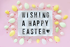 Traditional wishing Happy Easter on a light board around by colored Easter eggs and confetti