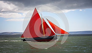 Traditional wooden boat with red sail.