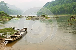 Traditional wooden boat tied at a river bank in rainy weather in Chengyang, Guangxi, China.